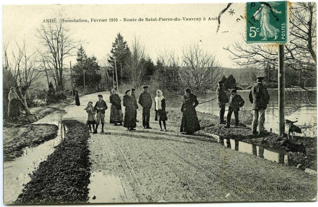 Carte postale 1910. Andé (27). Source : collection Archives Départementales 27. Personnages à pied observant le niveau de la Seine route de Saint Pierre du Vauvray
