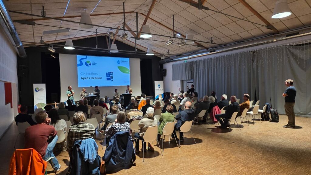 Public attentif devant un écran de projection de cinéma et devant les intervenants présents pour animer le débat